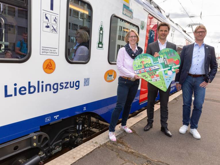 Drei Personen mit einem bunten Pappherz in der Hand vor einem Zug
